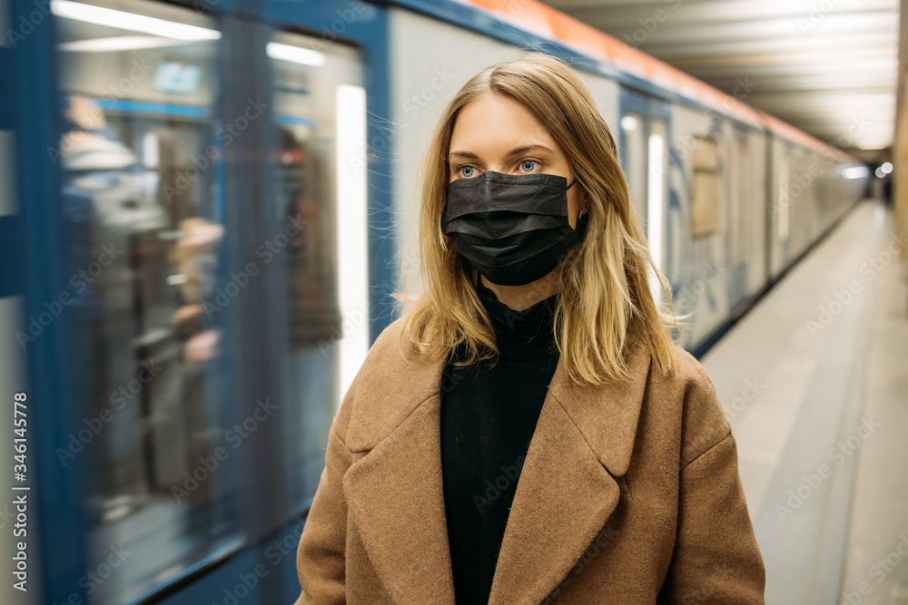 Blonde woman in black medical mask looking at camera while standing next to subway car. Blonde woman in black medical mask looking at camera while standing next to subway car.