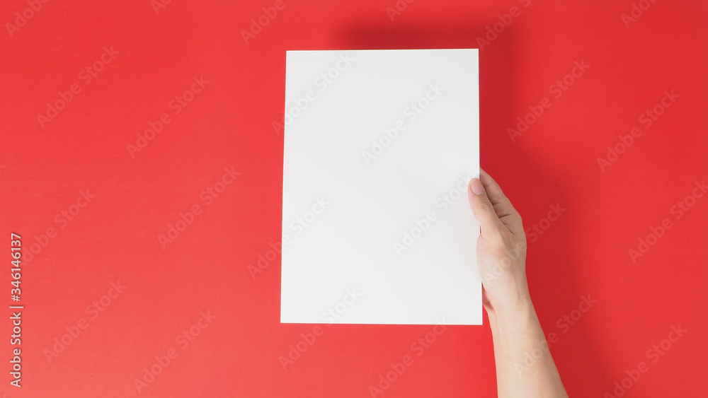 Right hand is holding white the A4 paper on red background. Right hand is holding white the A4 paper on red background.