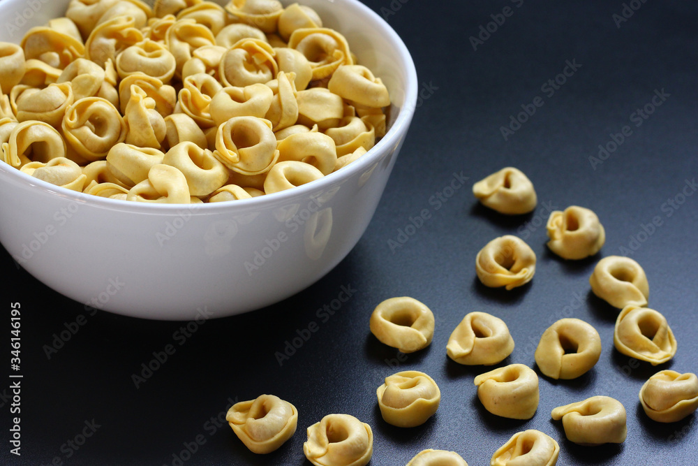 Tortellini, uncooked, in a white bowl on a dark metallic surface Tortellini, uncooked, in a white bowl on a dark metallic surface