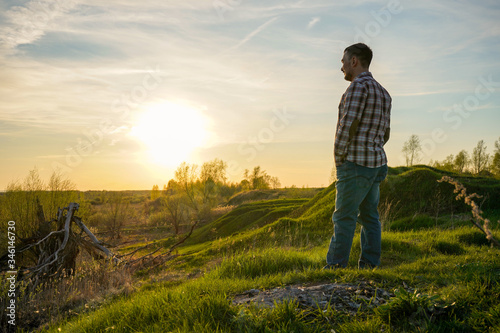 A man with a beard stands on a hill and looks at the sunset. © Сергей Храмов