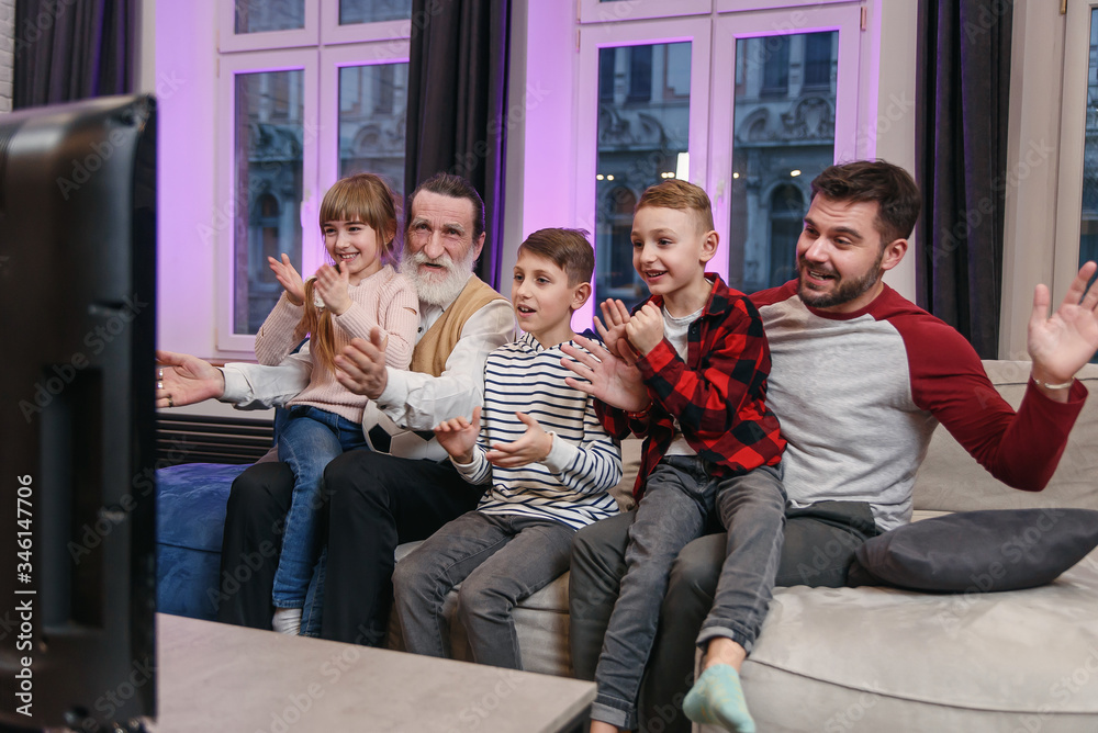 Happy friendly family watching football match, championship on the couch at home. Fans emotional cheering for favourite national team. Daddy, grandpa and grandchildren. Sport, TV, having fun.