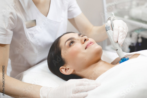 Side view of happy young woman lying on cosmetologist's table during rejuvenation procedure. Cosmetologist take care about neck skin youthfull and wellness.