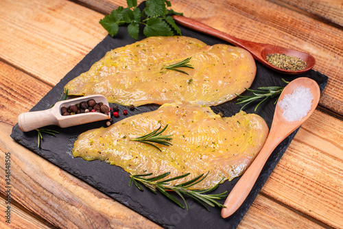 Sottilissime in marinade on a black stone kitchen board with spices, razmarin branch and a wooden spoon with salt on a wooden background. photo