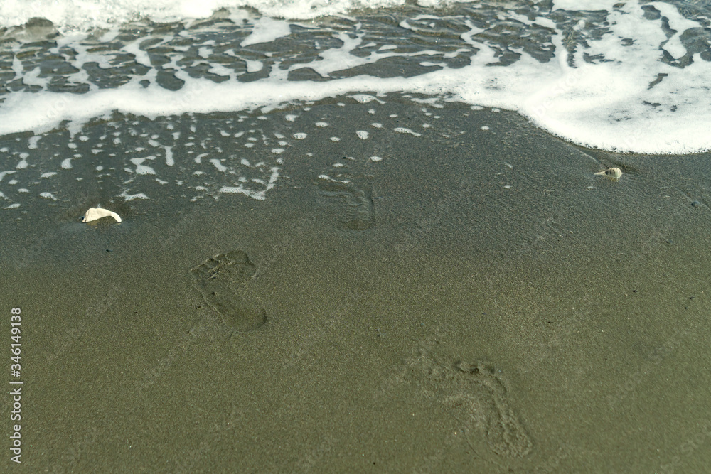 Footprints on wet sand beside a wave Footprints on wet sand beside a wave