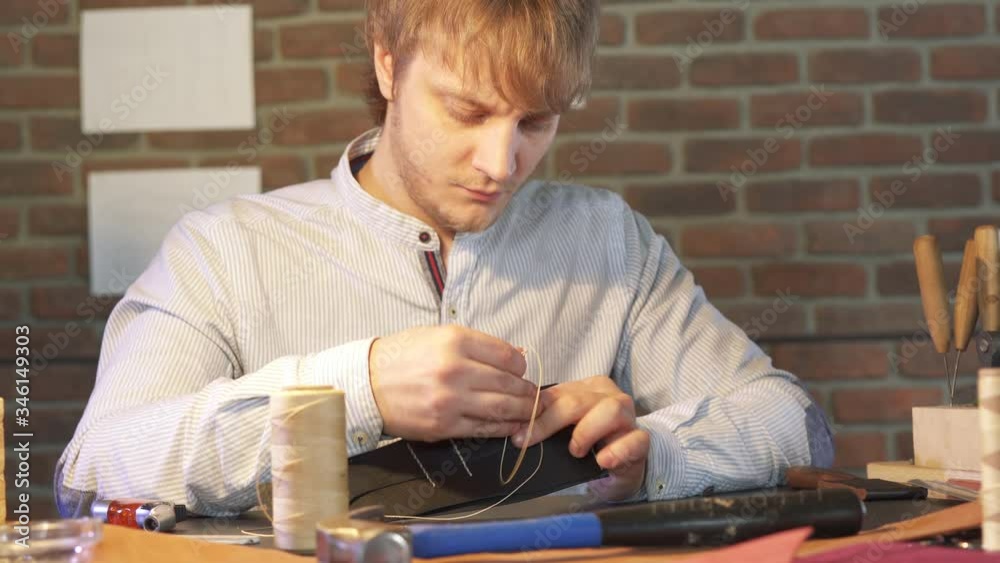 Young craftsman sews with a needle and thread by hand according to ...