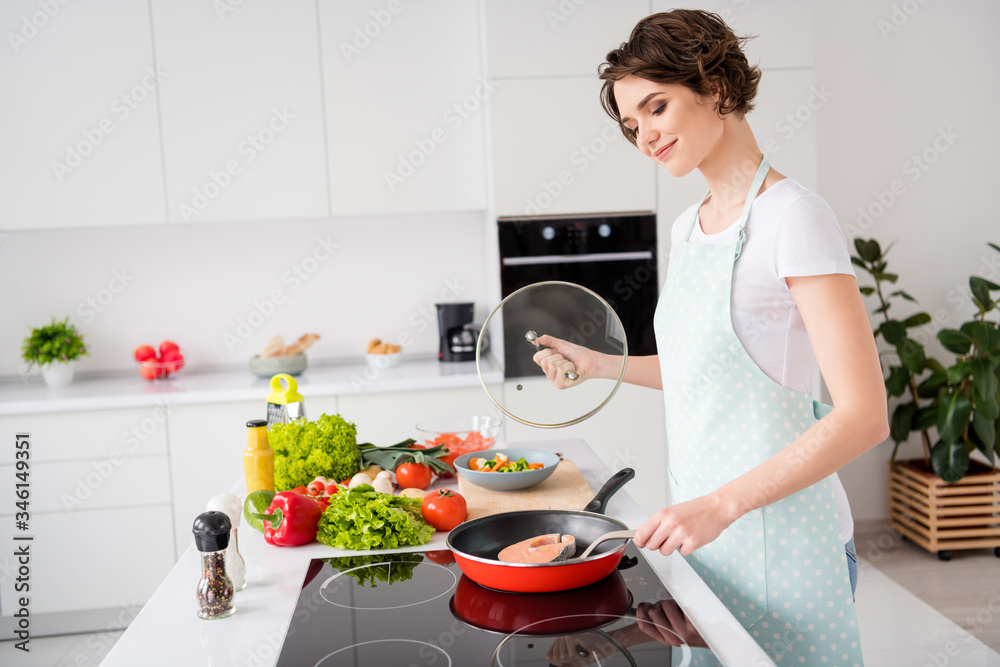 Profile photo of beautiful cheerful housewife lady put fresh raw salmon fillet steak on flying pan turning side dieting cooking hobby dinner wear apron stand modern kitchen indoors