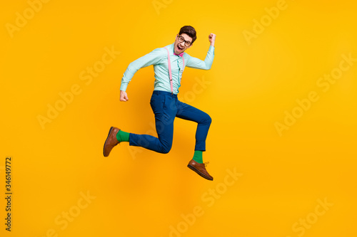 Full size profile photo of cool stylish guy jumping high up rejoicing winner wear specs shirt bow tie suspenders trousers shoes green socks isolated bright yellow color background