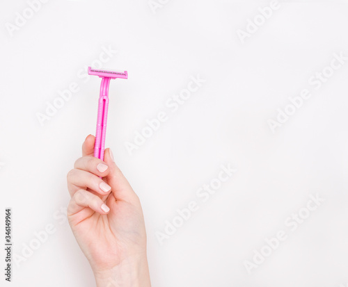 A woman's hand with a pink shaving machine. Light background, free space for text.