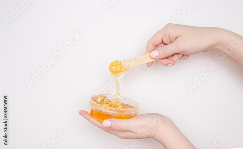 A woman's hand with a wooden spatula and sugar paste for depilation and a jar. Light background, copyspace.