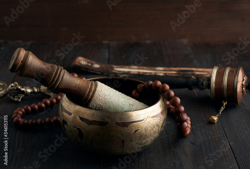 Tibetan singing copper bowl with a wooden clapper on a brown wooden table, objects for meditation and alternative medicine