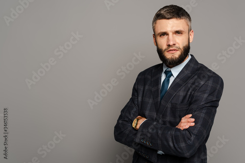 serious handsome bearded businessman in suit with crossed arms on grey background