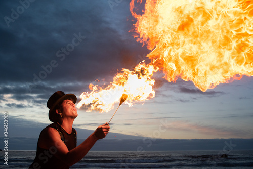 young man fire breathing on the beach at sunset. photo