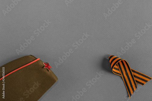 Flat lay of military uniform, cap, george ribbon are on a grey background. Concept of memory, symbol of Victory Day. Copy space. photo