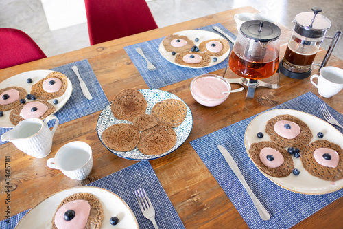 Thin whole grain pancakes on plates with yogurt and berries for family breakfast. Dining table set for tea or coffee break. Food concept