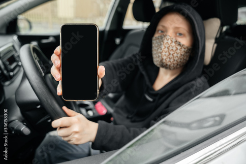 Female car driver shows a smartphone screen with a digital pass to travel through the city. The concept of the coronovirus epidemic.