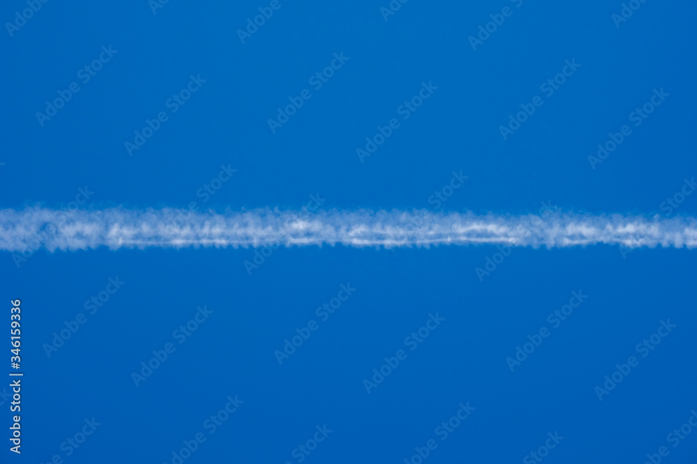 White jet passenger plane flying at high altitude in a blue clear cloudless sky. Behind the aircraft is a white condensation trail of water vapor.