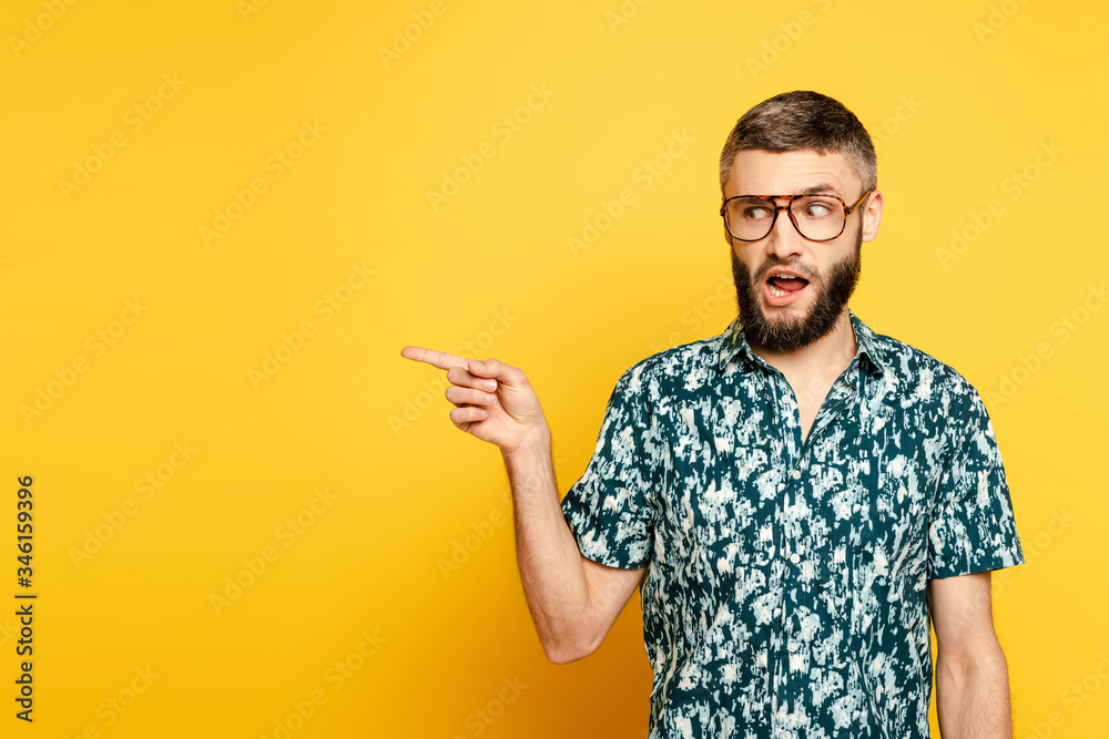 bearded guy in glasses pointing with finger aside on yellow - obrazy, fototapety, plakaty 