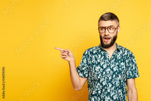 bearded guy in glasses pointing with finger aside on yellow