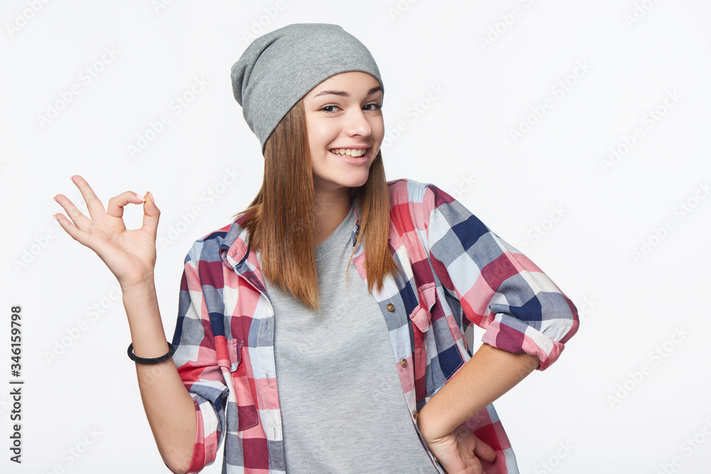 Happy teen girl wearing checkered shirt and beanie hat gesturing OK sign Happy teen girl wearing checkered shirt and beanie hat gesturing OK sign