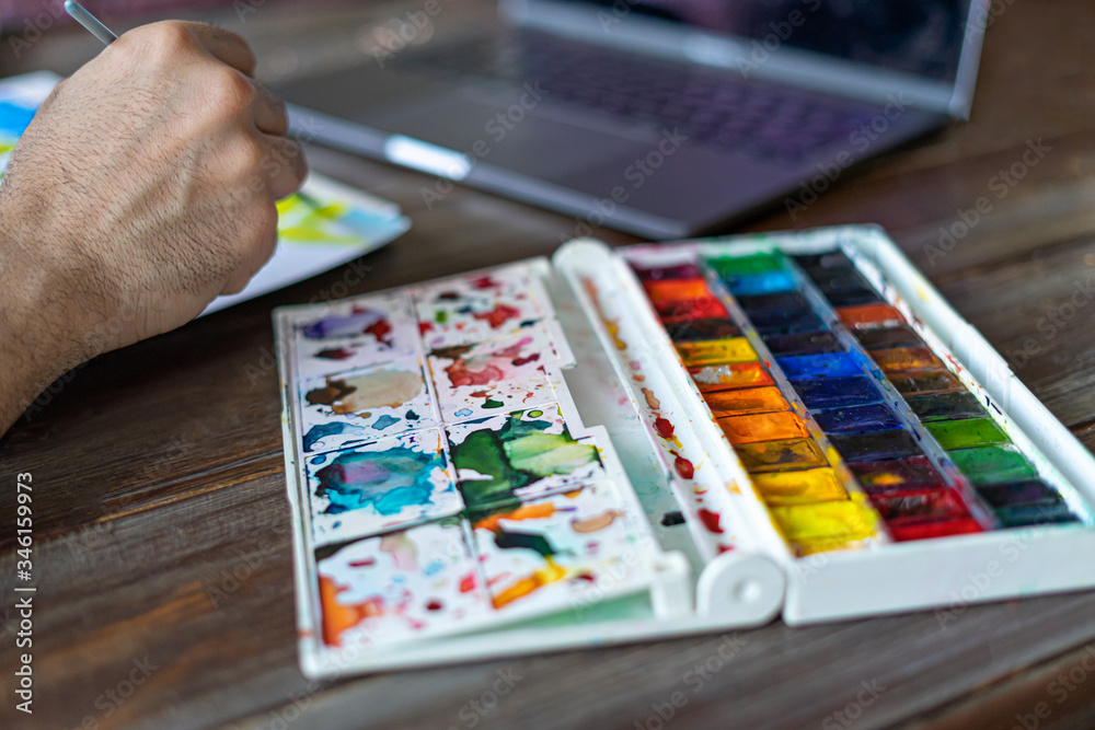 Fototapeta premium Painter artist using watercolor paints in front of laptop. online paiting learning aeducation.