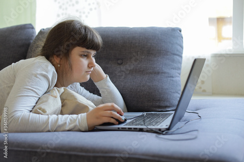 Caucasian girl laying on the sofa with laptop,lockdown at home during coronavirus