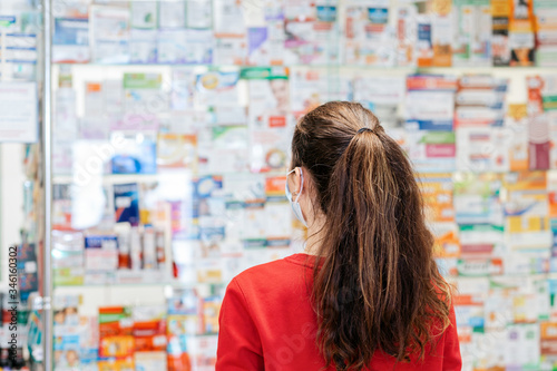 A brunette woman in a red sweater chooses medications at a pharmacy.In the background, the window is blurred. Copy space. Rear view. The concept of buying medicines in a pharmacy and a viral pandemic