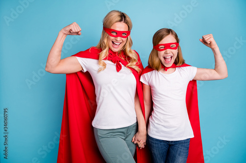 Photo of beautiful mom lady little daughter spend time together carnival super hero costumes showing strength muscles wear s-shirts red coat masks isolated blue color background
