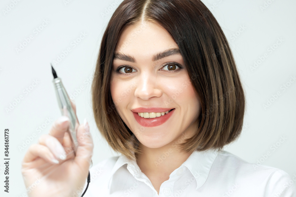 Microblading tools used for applying permanent eyebrow makeup. Brow tattoo application tools. Master holds in hands a professional apparatus for working with brows. Portrait of a girl with a smile. Microblading tools used for applying permanent eyebrow makeup. Brow tattoo application tools. Master holds in hands a professional apparatus for working with brows. Portrait of a girl with a smile.
