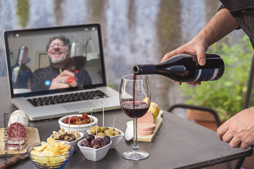 Aperitif video call party. Adult men are making a pre-meal aperitif with snacks  wine  and Italian appetizers together at home using teleconference platform apps.