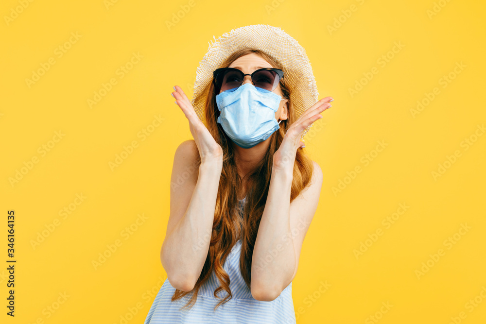 Shocked girl in a summer hat and sunglasses, wears a medical protective mask against a viral infection, on a yellow background. Quarantine, coronavirus, summer