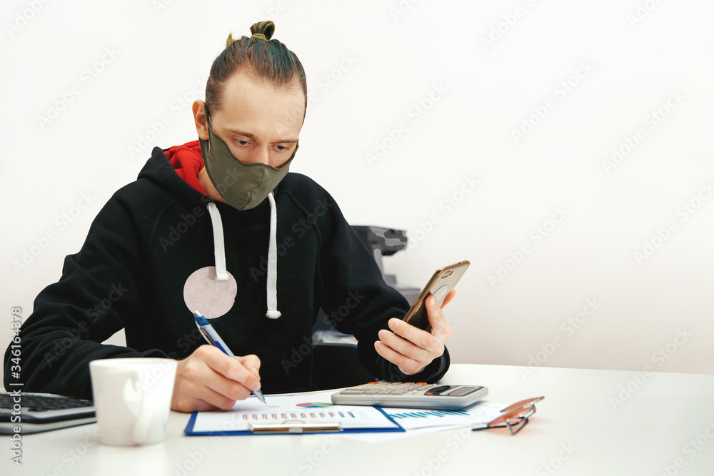 A young specialist in a protective mask works with financial documents A young specialist in a protective mask works with financial documents