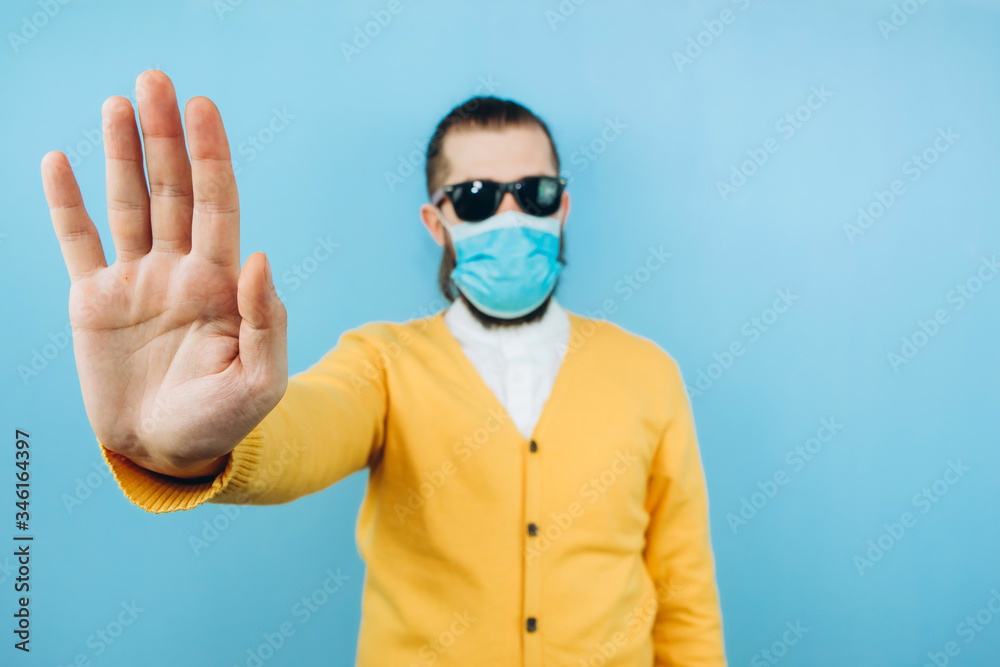 a man with glasses and a medical mask on a blue background. An emotional and positive guy on self-isolation. Coronavirus. Studio shooting. Pandemic COVID 19.