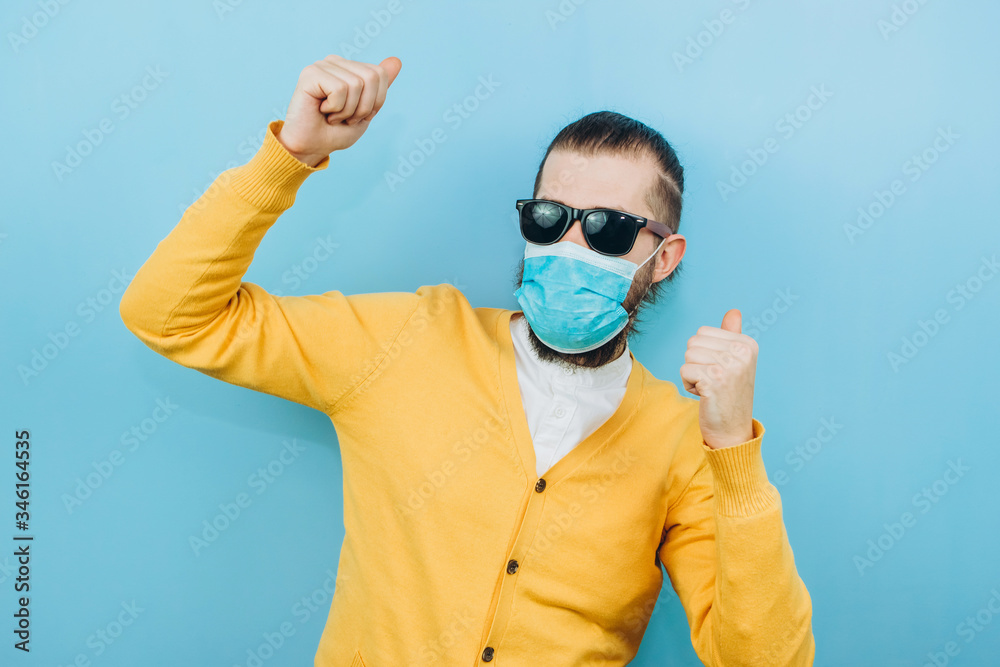 a man with glasses and a medical mask on a blue background. An emotional and positive guy on self-isolation. Coronavirus. Studio shooting. Pandemic COVID 19. a man with glasses and a medical mask on a blue background. An emotional and positive guy on self-isolation. Coronavirus. Studio shooting. Pandemic COVID 19.