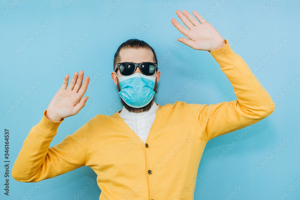 Naklejka premium a man with glasses and a medical mask on a blue background. An emotional and positive guy on self-isolation. Coronavirus. Studio shooting. Pandemic COVID 19.