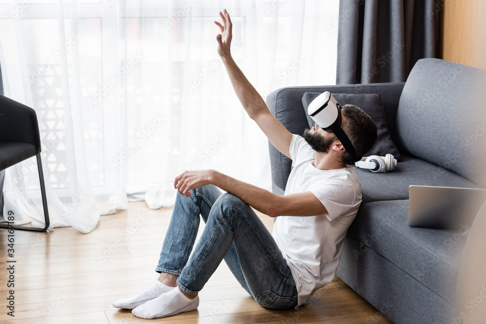 Side view of man using vr headset near laptop and headphones on couch Side view of man using vr headset near laptop and headphones on couch