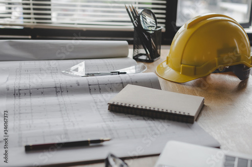 construction working tool, blueprint and yellow safety helmet on architect workplace desk in meeting room office center at construction site, construction, engineering tools and architectural concept