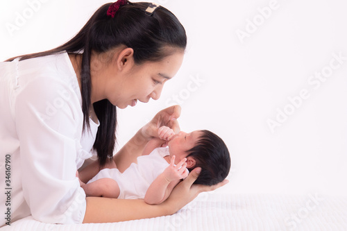 Close up beautiful young Asian mother kissing and hold tiny adorable newborn baby girl 0-1 month on white bed with caring and love, lifestyle health care newborn at home concept on white background
