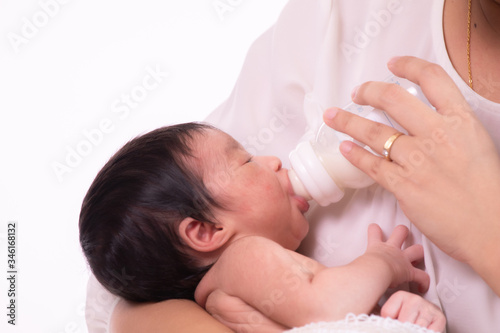 Beautiful Asian mother hold newborn 0-1 month baby infant on her breast feeding milk by bottle, adorable baby look to her mother safety and comfortable, mother nurturing at home, motherhood task