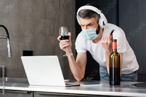 Fényképezés Pensive man in headphones and medical mask holding usb flash drive and glass of