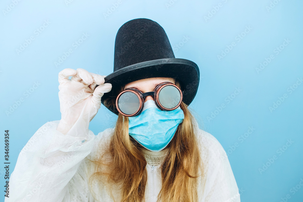 Creative girl in a white robe, medical mask, glasses and a hat on a blue background. Self-isolation during coronavirus quarantine. Epidemic covid-2019.
