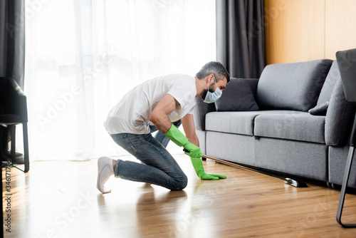 Side view of man in medical mask cleaning floor at home