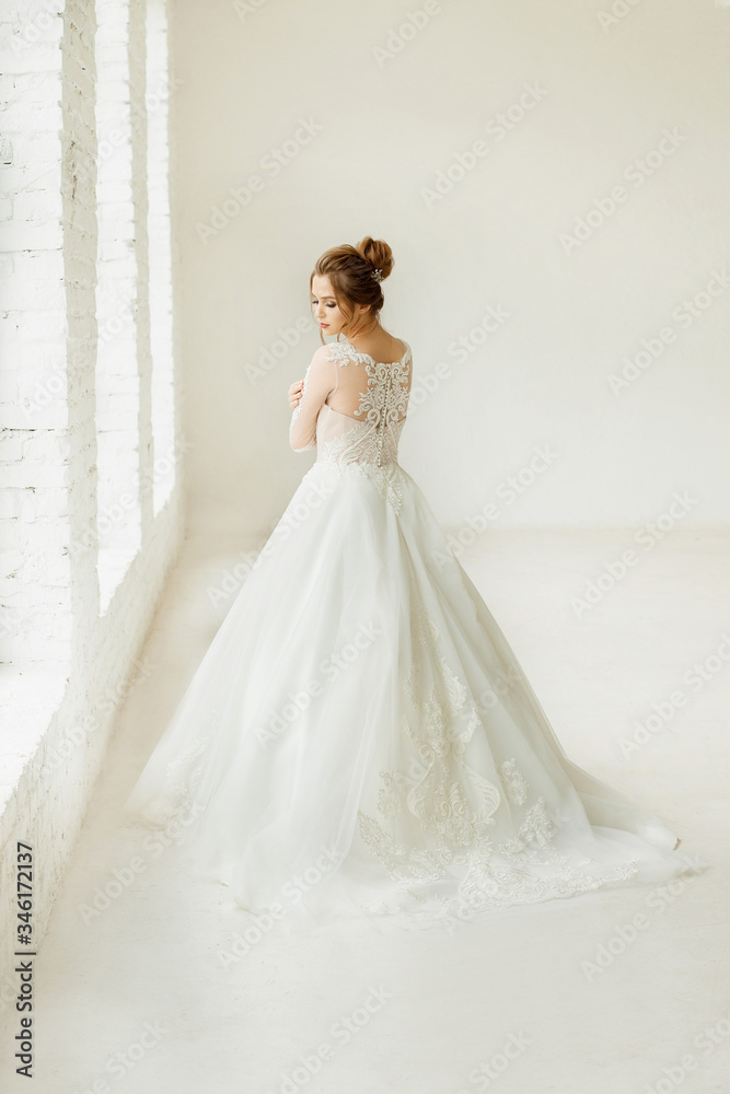 bride in white wedding dress. happy beautiful young woman in white traditional wedding dress on white background. big windows and white walls.