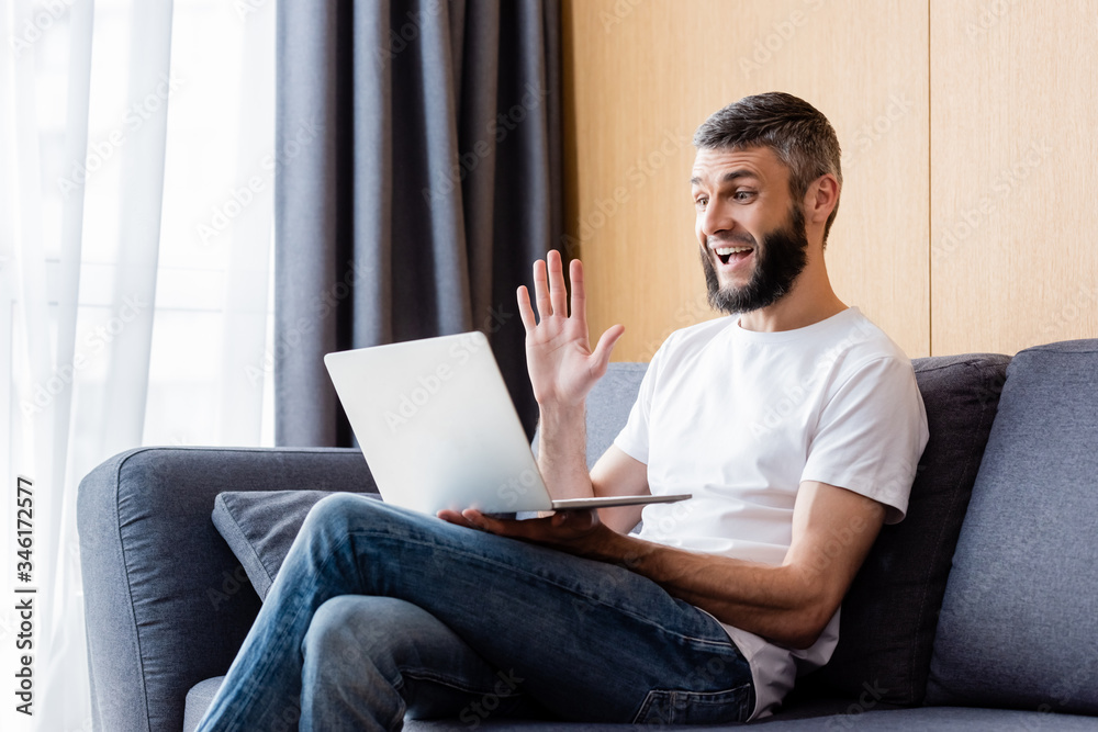 Side view of positive teleworker having video chat on laptop in living room Side view of positive teleworker having video chat on laptop in living room
