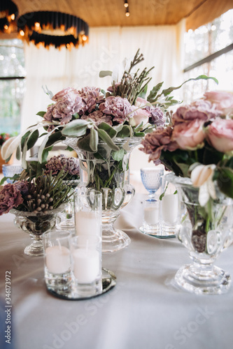 Fototapeta Naklejka Na Ścianę i Meble -  Wedding decor in purple and gray. Banquet tables with tablecloths are decorated with compositions of flowers, on the tables are plates, glasses and candles