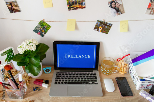 The laptop is on the table. Near the phone, cup, and cosmetics. On screen Freelance photo