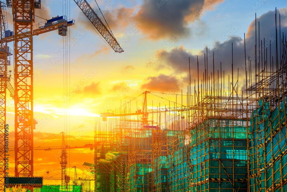 Tower crane and building construction site silhouette at sunrise.