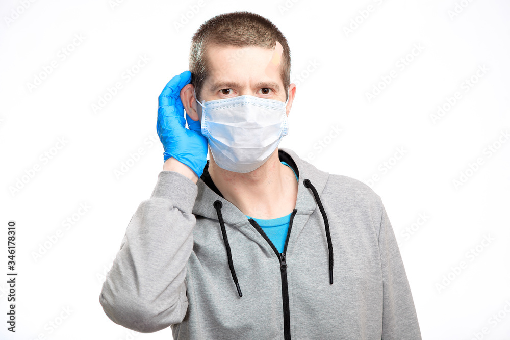 curious man eavesdrops, put his hand to the ear to hear better. Dressed in a medical mask, rubber gloves, sports jacket, looks into the camera. Close-up, isolated