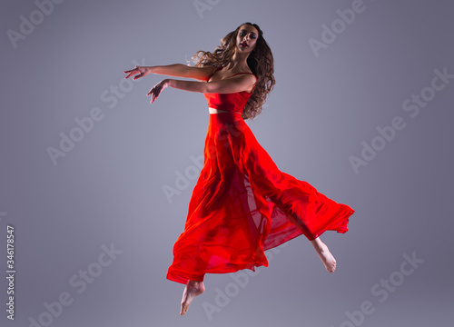 jumping professional dancer girl isolated on gray background. Woman in red dress