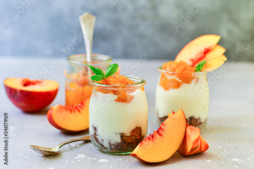 yogurt with peach jam and fresh peaches in a round glass jar on a gray background, dessert recipe. healthy breakfast ,  selective focus