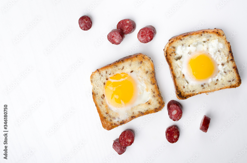 Top view of two eggs in the baskets and tasty fried pieces of sausages on the white background.Traditional breakfast
